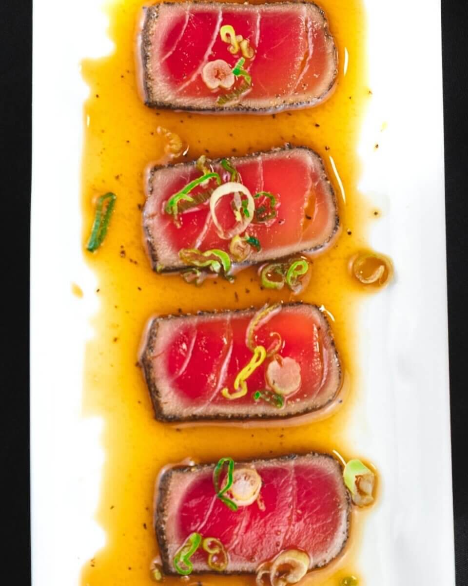 13 New Birmingham Restaurants to Try This Month - 10 Four slices of seared ahi tuna are arranged in a row on a white plate, topped with sliced green onions and served in a soy-based sauce—a standout dish at one of the new restaurants Birmingham food lovers must try.