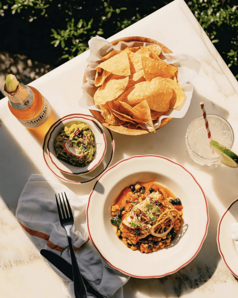 15+ Birmingham Restaurants Open on July 4th - 12 A plate of grilled fish with vegetables, tortilla chips, guacamole, a cocktail with lime, and a bottle of beer on a white table—perfect for July 4th at open Birmingham restaurants.