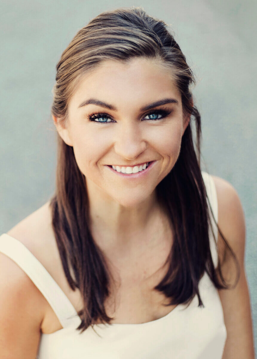 This BHAM Founder Believes That Movement is Medicine - 2 A woman with long brown hair, blue eyes, and a white sleeveless top smiles while looking up at the camera.