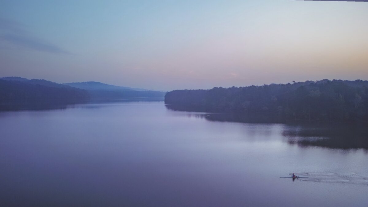 8 Ways to Get on the Water around BHAM, All Within an Hour’s Drive - 6 A lone rower glides across the calm, wide Lake Purdy at dawn near BHAM, enjoying peaceful water activities beneath a pastel sky, with tree-lined shores and distant hills in view.
