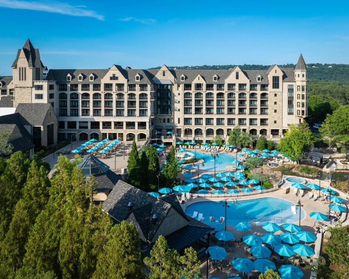 8 Ways to Get on the Water around BHAM, All Within an Hour’s Drive - 7 The Ross Bridge Resort hotel with stone architecture and outdoor swimming pools surrounded by sun loungers and blue umbrellas, set among green trees.