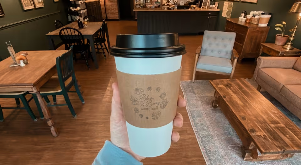 Where to Eat & Sip in Gatlinburg: From Local Favorites to Hidden Gems - 3 A hand holds a takeaway coffee cup in a cozy coffee shop with wooden furniture, tables, and chairs—perfect for relaxing after exploring Gatlinburg restaurants.