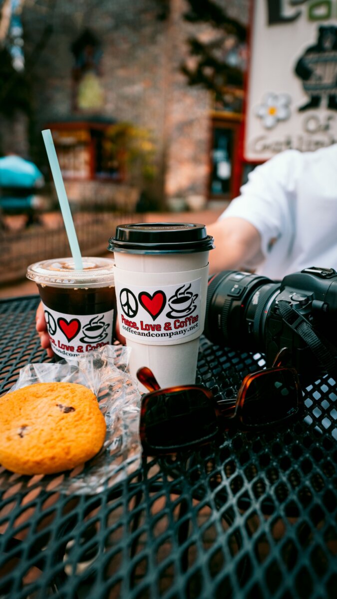 Where to Eat & Sip in Gatlinburg: From Local Favorites to Hidden Gems - 4 A close-up of two drinks, a cookie, sunglasses, and a camera on a metal table outdoors, capturing the relaxed vibe of Gatlinburg dining as a person's arm reaches toward the items.