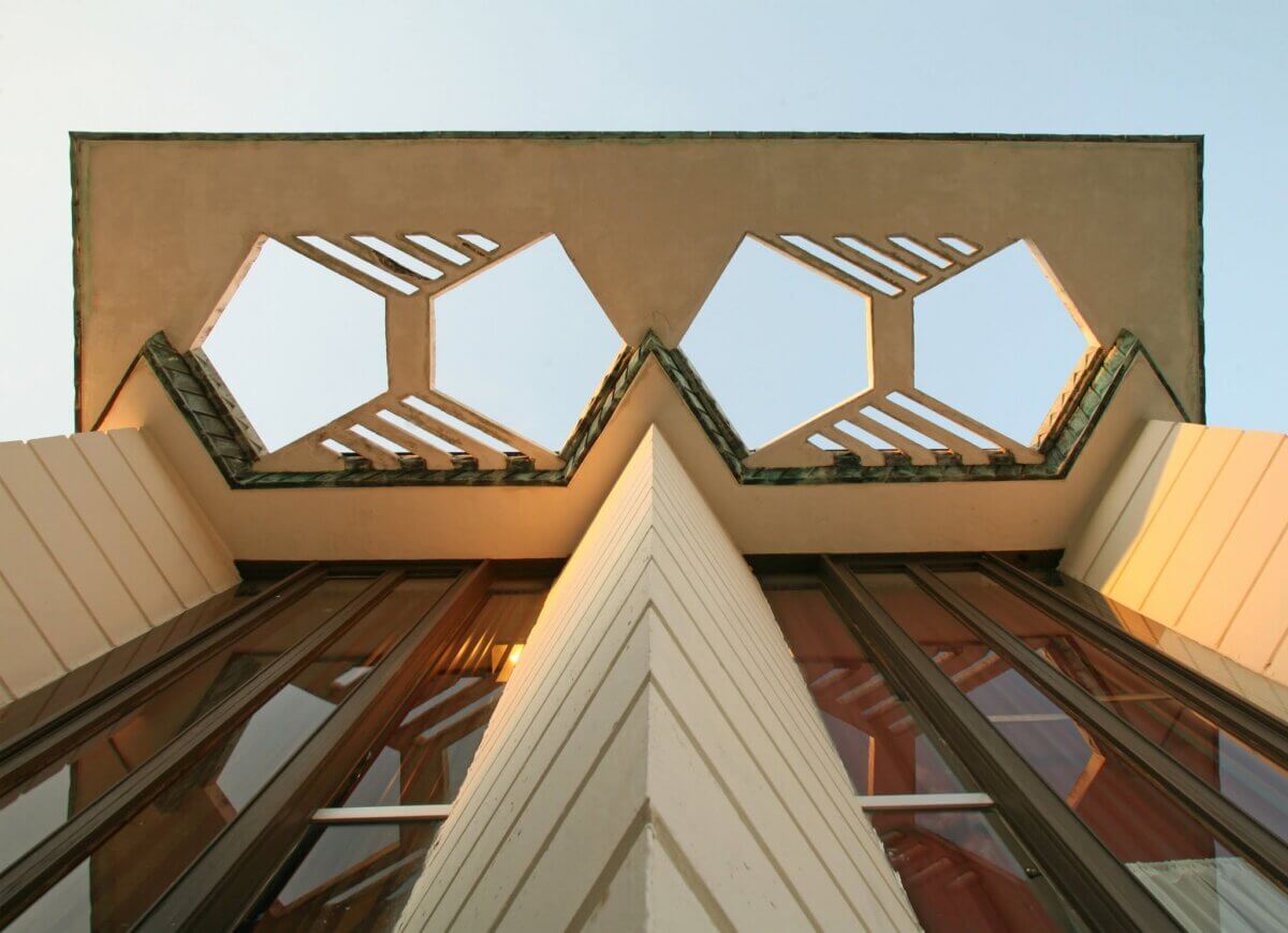 Low-angle view of a modern building facade with geometric cut-out shapes and reflective windows, set against a clear sky in the South.