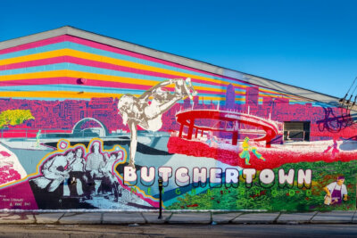A colorful mural on a building wall in Butchertown Louisville features skateboarders, a group of people, city buildings, and large text reading "BUTCHERTOWN LEGENDHOOD.