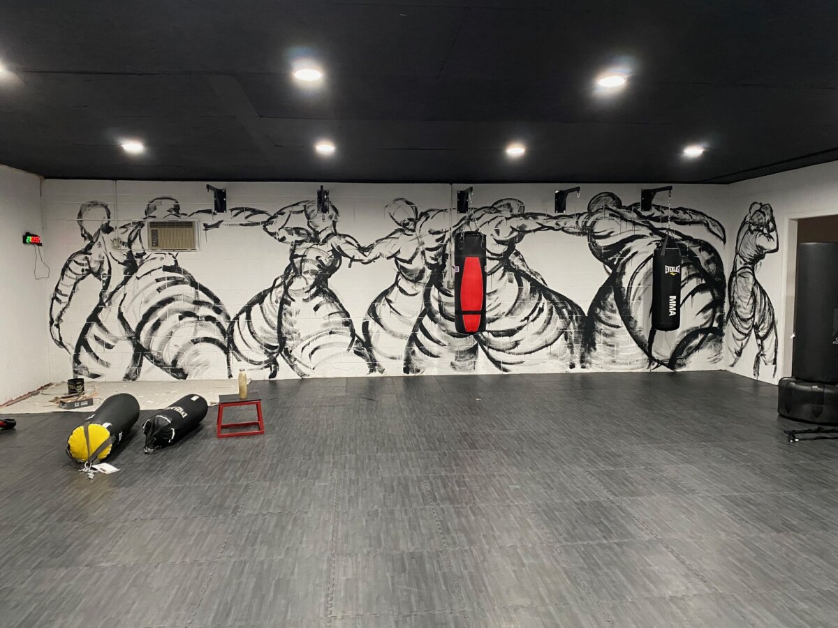 How Louisville Artist Robyn Gibson Turns Boxing Into Art - 6 A gym in Louisville featuring a mural of boxers, punching bags hanging and lying on the floor, and gym equipment scattered around—a creative touch inspired by Robyn Gibson.