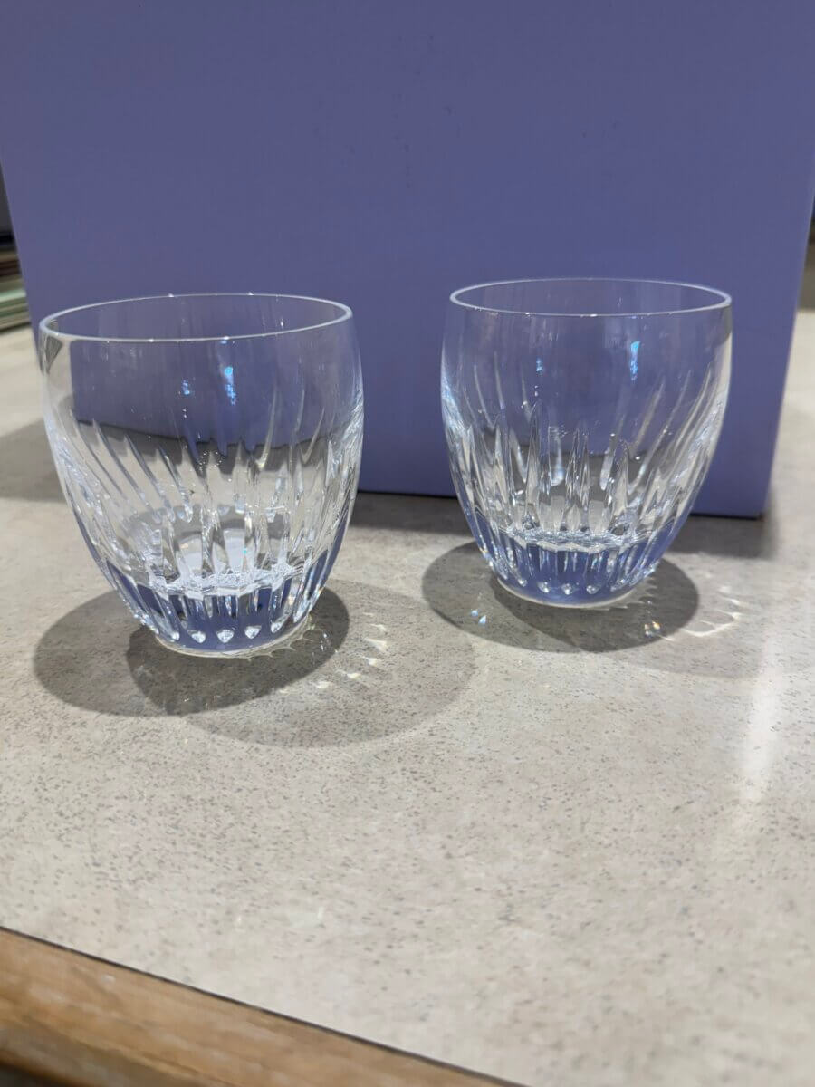 16 Luxe Louisville FINDS for July: Fine Art, Rare Bourbon & Resort-Ready Style - 6 Two clear, empty glass tumblers with a textured pattern sit on a light-colored countertop in front of a light purple background—an elegant touch to any Luxe Louisville gathering this July.