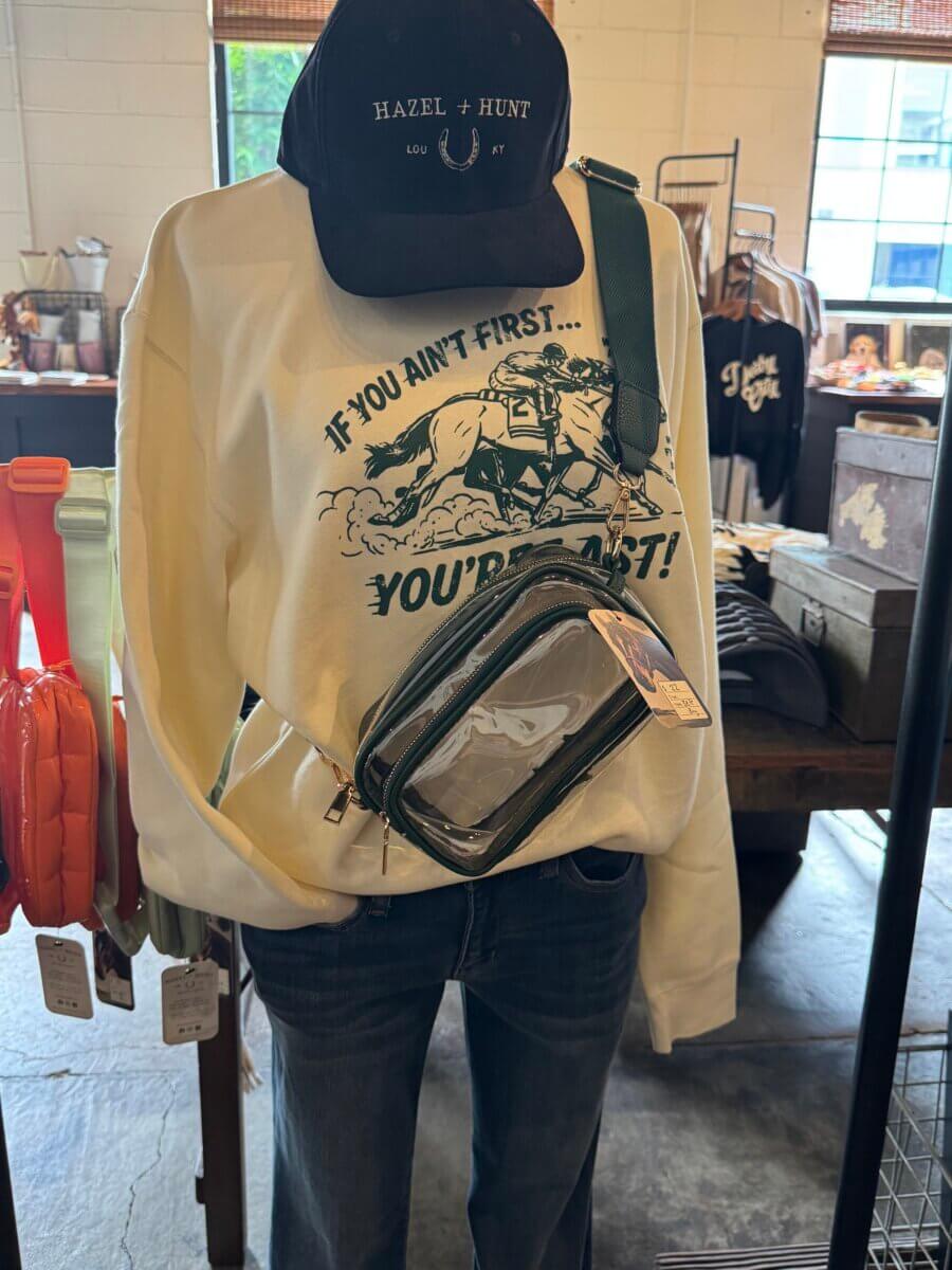 16 Louisville FINDS for June: Summer Style, Tabletop Charm & Little Luxuries - 8 A mannequin dressed in a printed sweatshirt, jeans, a black cap, and a clear crossbody bag showcases one of this season’s summer picks at Louisville FINDS.