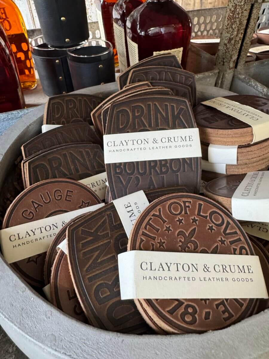 16 Louisville FINDS for June: Summer Style, Tabletop Charm & Little Luxuries - 14 A selection of round leather coasters with embossed text and designs, branded as Clayton & Crume handcrafted leather goods, displayed in a round container—perfect for everyday picks or unique Louisville finds.