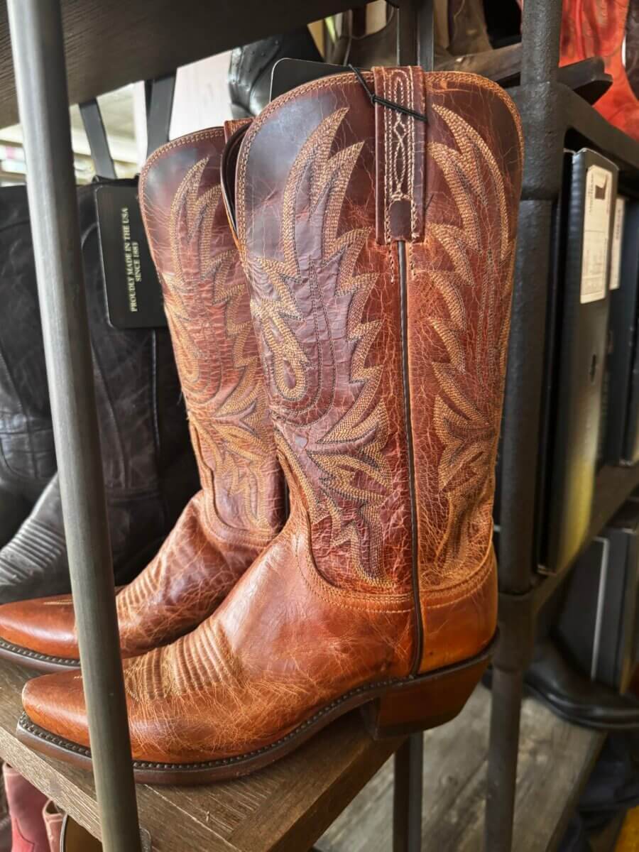 16 Luxe Louisville FINDS for July: Fine Art, Rare Bourbon & Resort-Ready Style - 13 A pair of brown leather cowboy boots with decorative stitching, part of the Louisville Finds July collection, displayed on a wooden shelf.