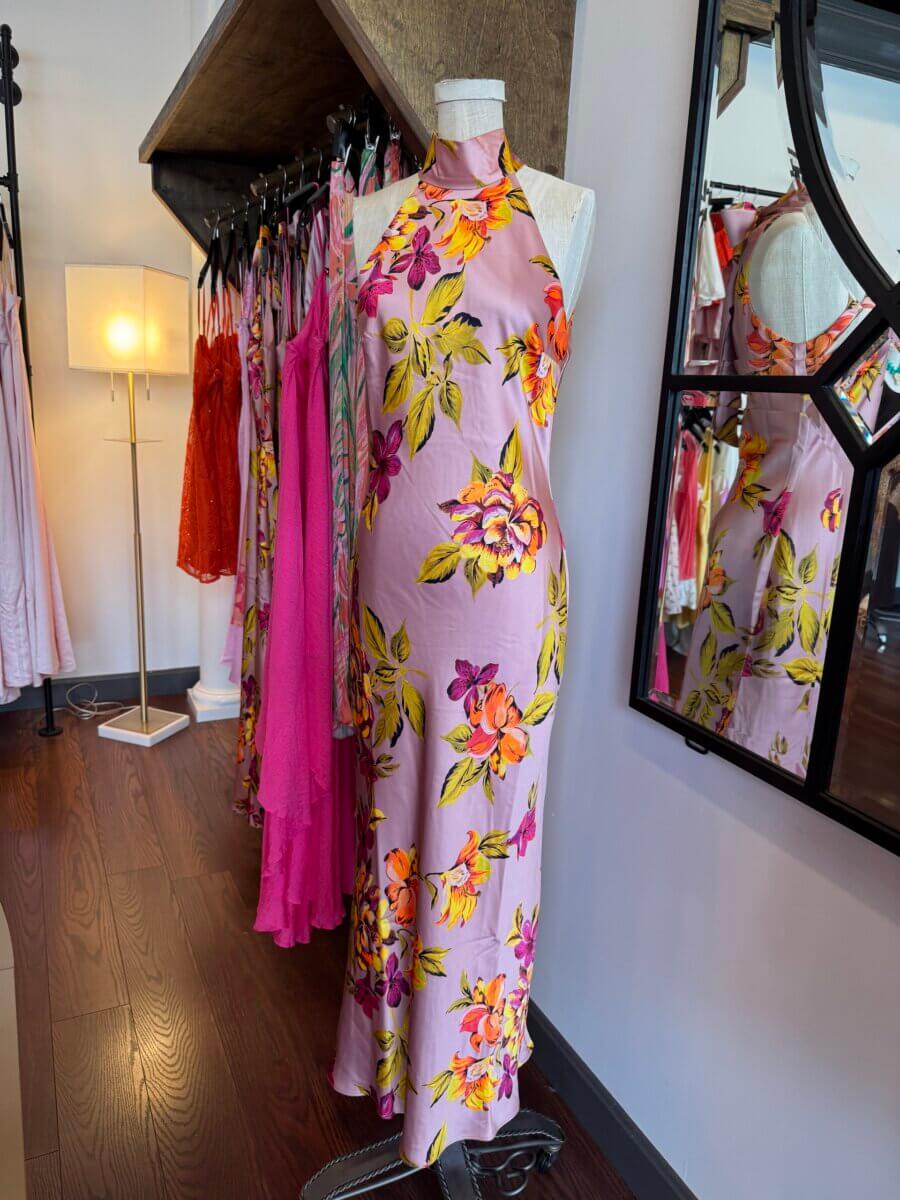 16 Louisville FINDS for June: Summer Style, Tabletop Charm & Little Luxuries - 5 A mannequin displays a sleeveless, high-neck, pink floral dress—one of our top June picks—in a clothing boutique with dresses hanging on racks in the background.