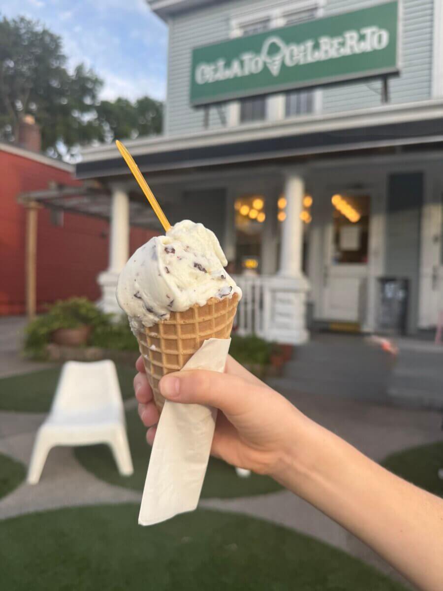 16 Louisville FINDS for June: Summer Style, Tabletop Charm & Little Luxuries - 16 A hand holds a waffle cone with a scoop of gelato and a yellow spoon in front of a building with a sign reading "Gelato Gilberto"—one of Louisville’s everyday luxuries and perfect for your summer picks.