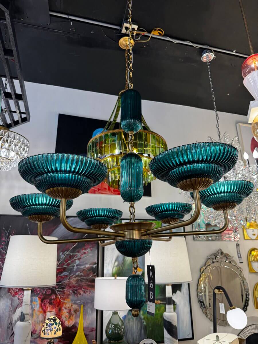 16 Luxe Louisville FINDS for July: Fine Art, Rare Bourbon & Resort-Ready Style - 4 A large chandelier with teal and green glass accents and nine arms shines in a Luxe Louisville lighting store, surrounded by lamps, mirrors, and paintings—a stunning July highlight among unique Louisville finds.