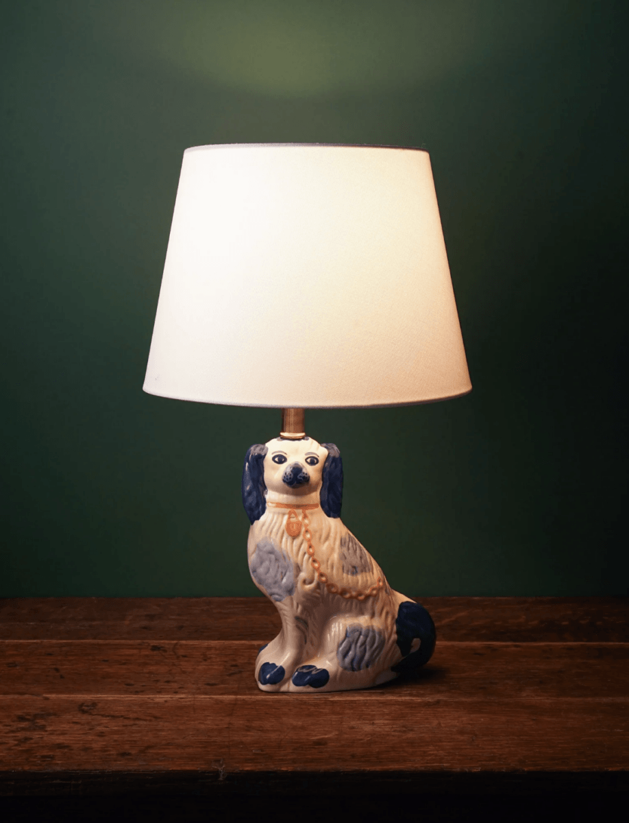 16 Louisville FINDS for June: Summer Style, Tabletop Charm & Little Luxuries - 12 A table lamp with a white shade and a ceramic base shaped like a dog, featured among our June picks for Louisville FINDS, sits on a wooden surface against a green background—perfect for adding summer luxuries to your home décor.