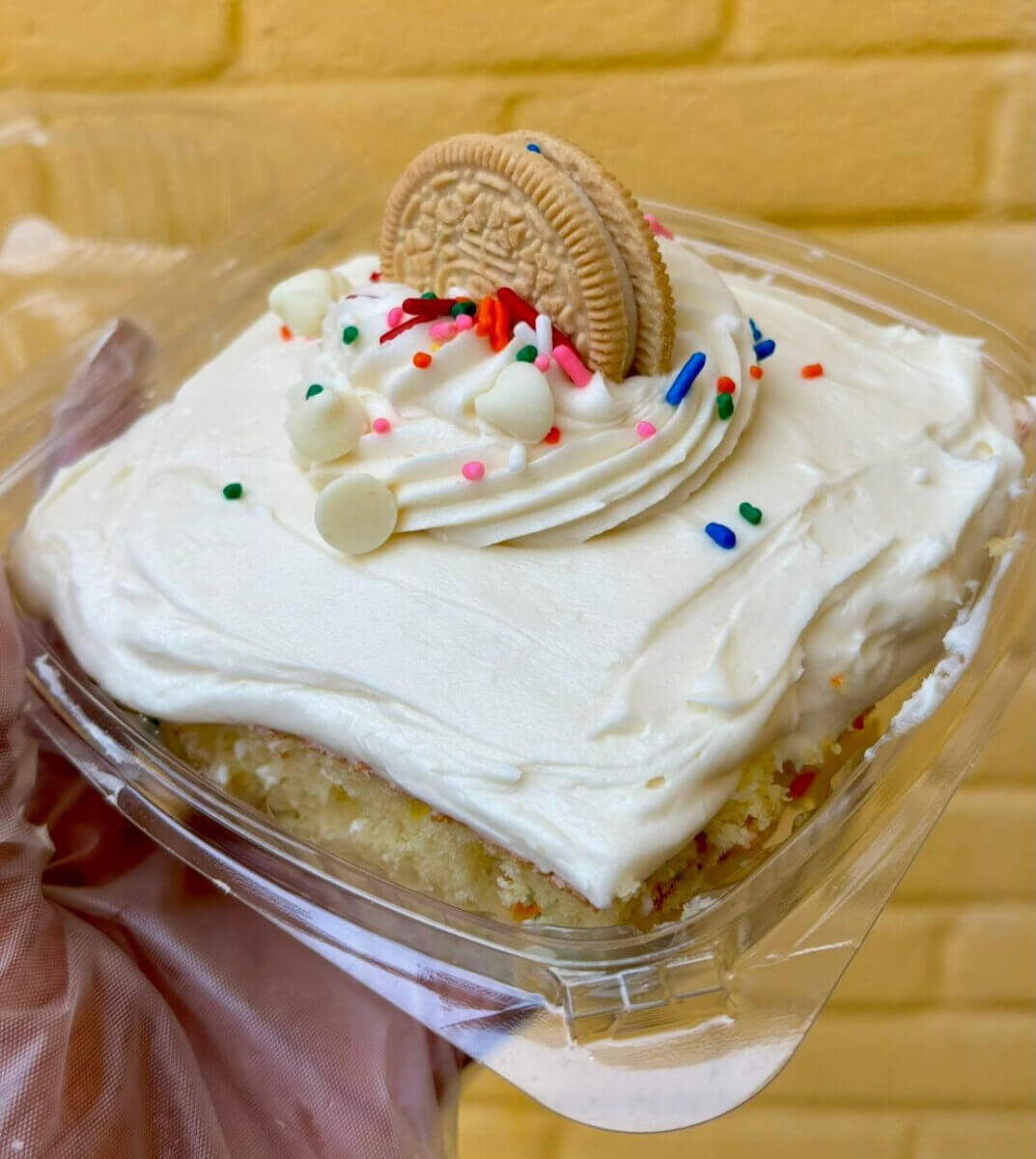 3 New Louisville Restaurants to Try (+2 New Menus!) - 3 A square slice of vanilla cake with white frosting, topped with sprinkles, white chocolate chips, and a golden sandwich cookie, in a clear plastic container.