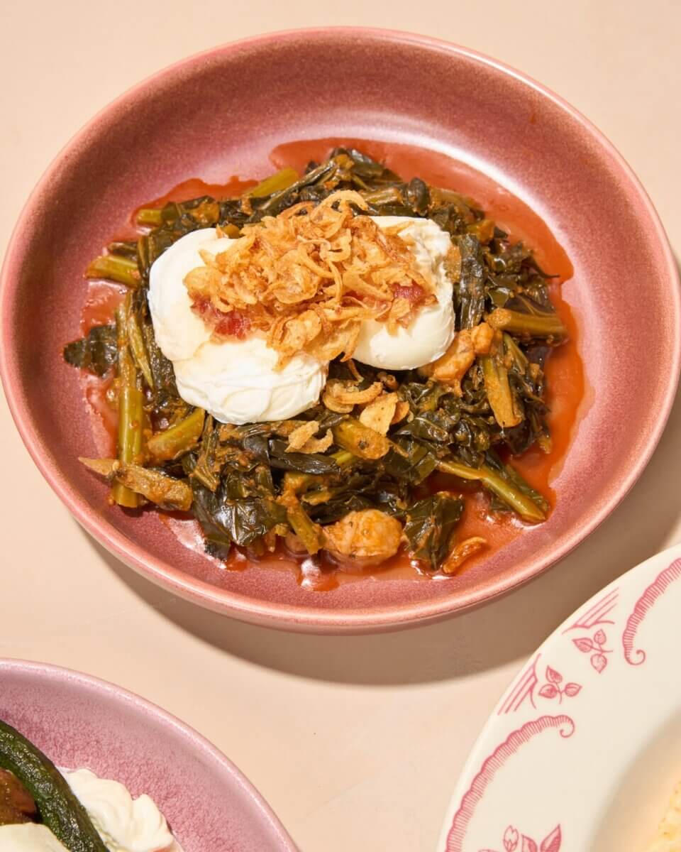 3 New Louisville Restaurants to Try (+2 New Menus!) - 6 A pink bowl filled with stewed greens, topped with two poached eggs and crispy fried onions, sits on a light-colored surface—a vibrant dish inspired by new menus at top Louisville restaurants.