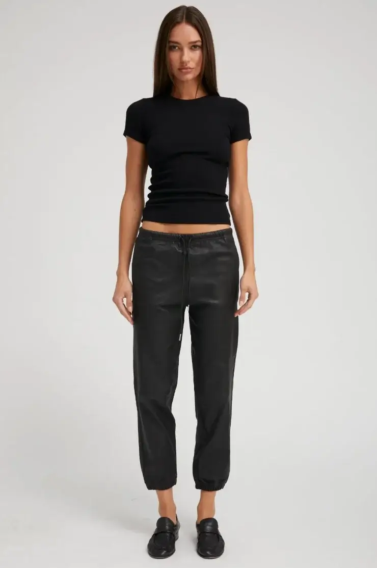 17 Luxurious Birmingham FINDS: Polished Summer Style, Artful Decor & Everyday Luxuries - 8 A woman stands facing forward, wearing a fitted black t-shirt, black jogger pants, and black shoes against a plain light background—an effortlessly chic summer look inspired by luxurious Birmingham style.