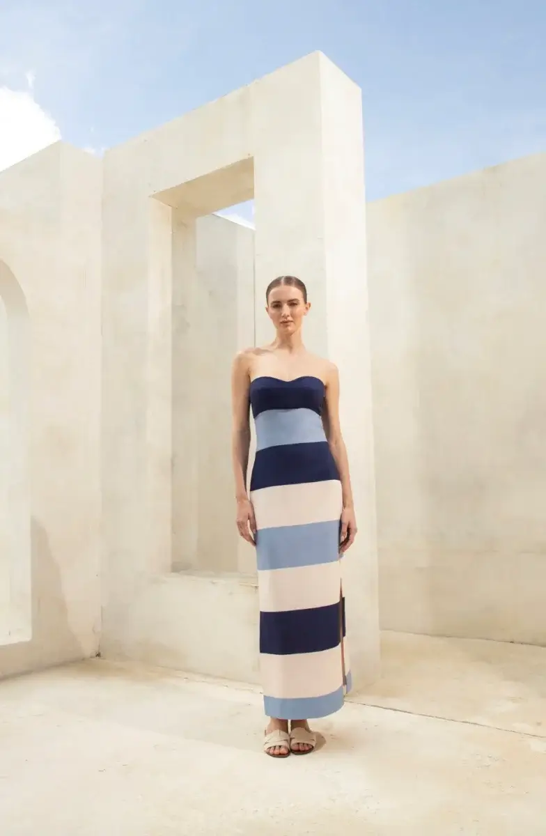 17 Luxurious Birmingham FINDS: Polished Summer Style, Artful Decor & Everyday Luxuries - 9 A woman stands outside against a cream-colored wall in a strapless, ankle-length dress with wide horizontal blue, white, and beige stripes—a perfect summer look from FINDS in luxurious Birmingham.