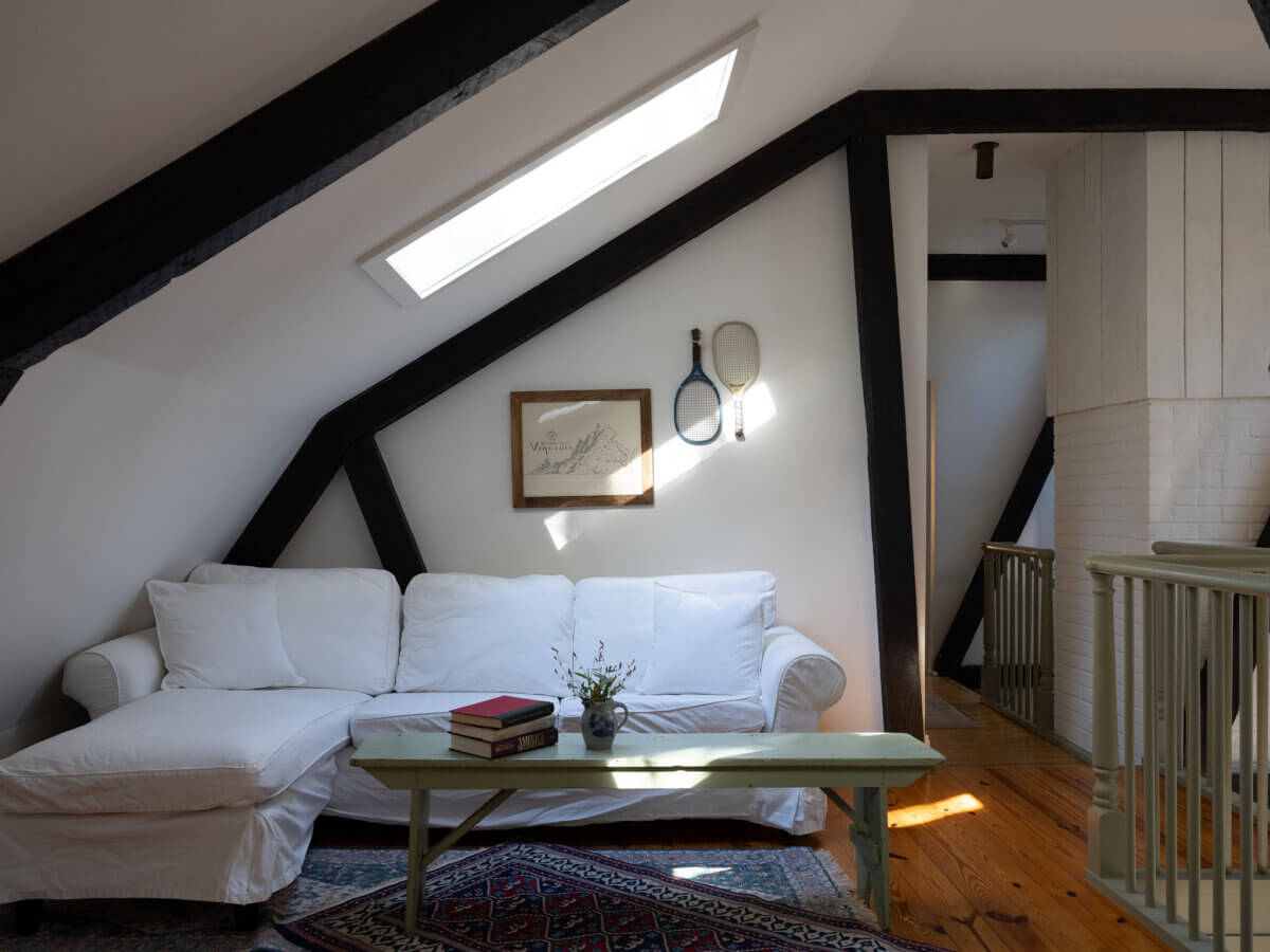 A white sectional sofa sits under a skylight in an attic room with exposed beams, wooden floors, and framed decor—bringing cozy charm into a stylish modern space.