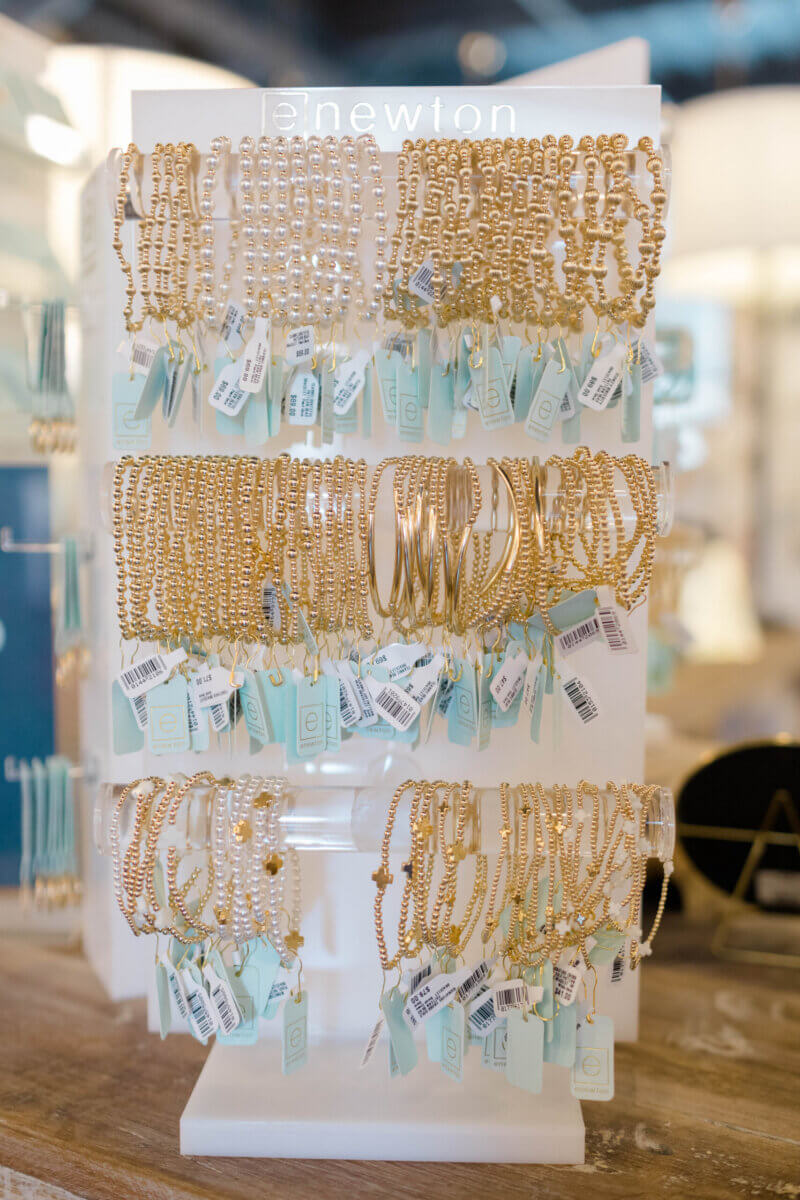 15 Memphis FINDS to Kick Off Summer: Vacation-Ready Style & More - 11 Display stand with several rows of gold bracelets and beaded jewelry, each with price tags, set on a wooden surface in a well-lit store—perfect for those seeking unique Mother's Day gift ideas.