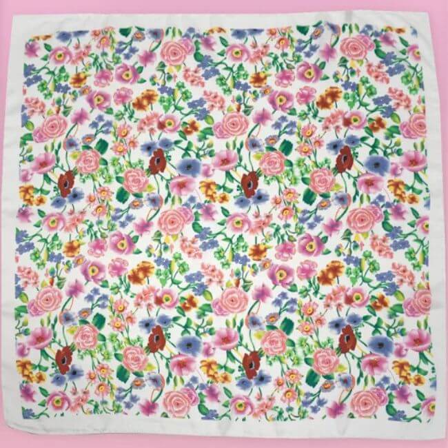 15 Memphis FINDS to Kick Off Summer: Vacation-Ready Style & More - 12 A square white scarf with a colorful floral pattern featuring pink, red, purple, and blue flowers, perfect for adding flair to your Memphis shopping adventures, displayed on a pink background.
