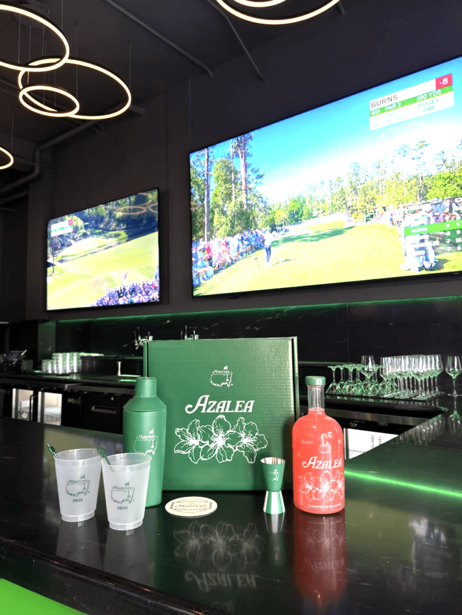 A bar counter displays branded Azalea cocktail items and a pink drink, with two TVs in the background showing a golf tournament.