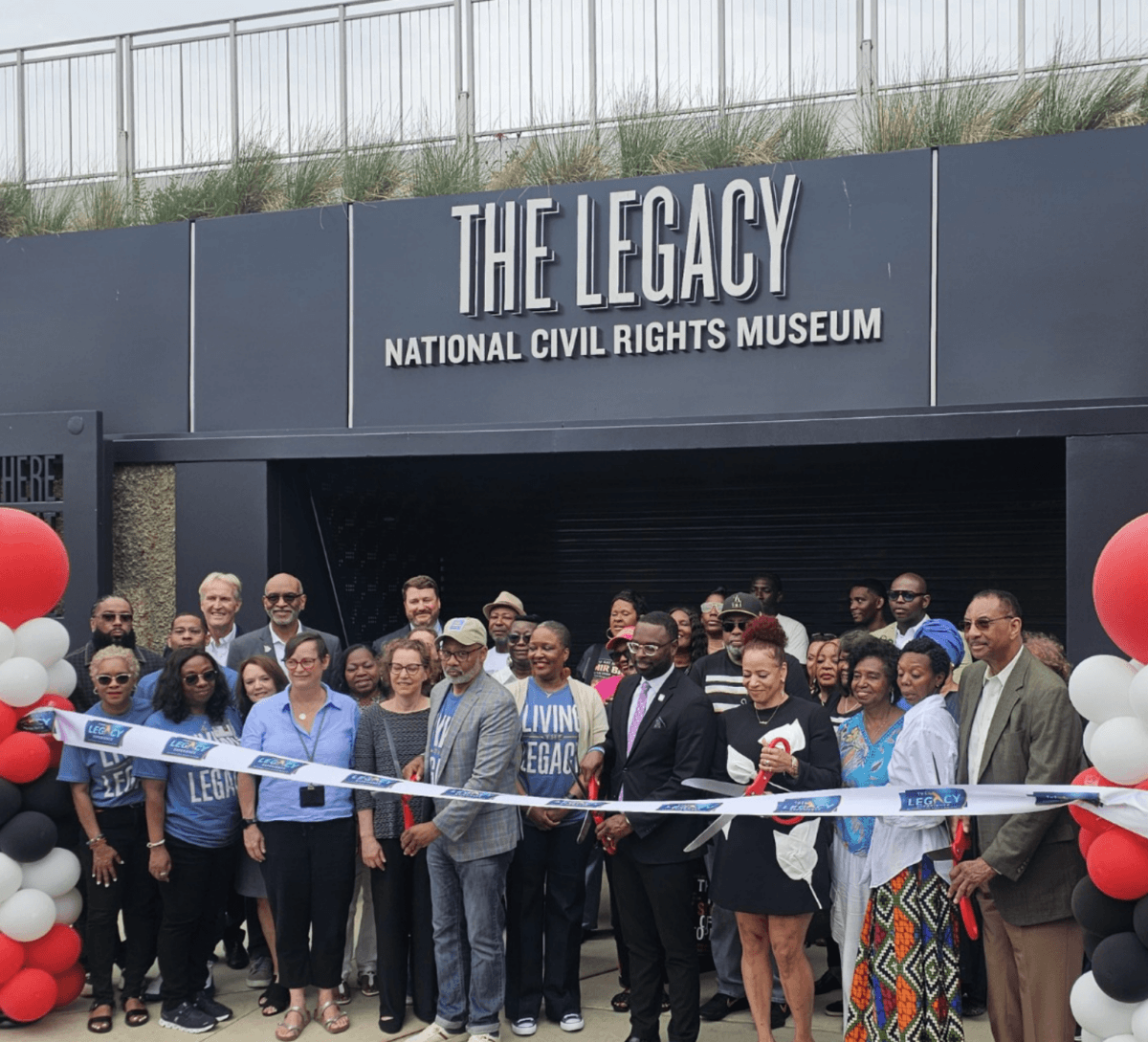 The South’s Biggest Museum Boom is Happening in Memphis - 4 A group of people, some holding a ribbon, stand in front of The Legacy National Civil Rights Museum for a ribbon-cutting ceremony, surrounded by red, white, and black balloons.