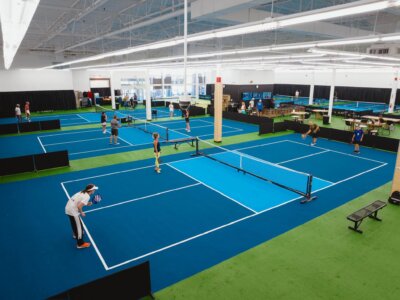 Players enjoy pickleball on multiple indoor courts with blue surfaces and green flooring in Memphis; benches and tables are arranged around the courts.