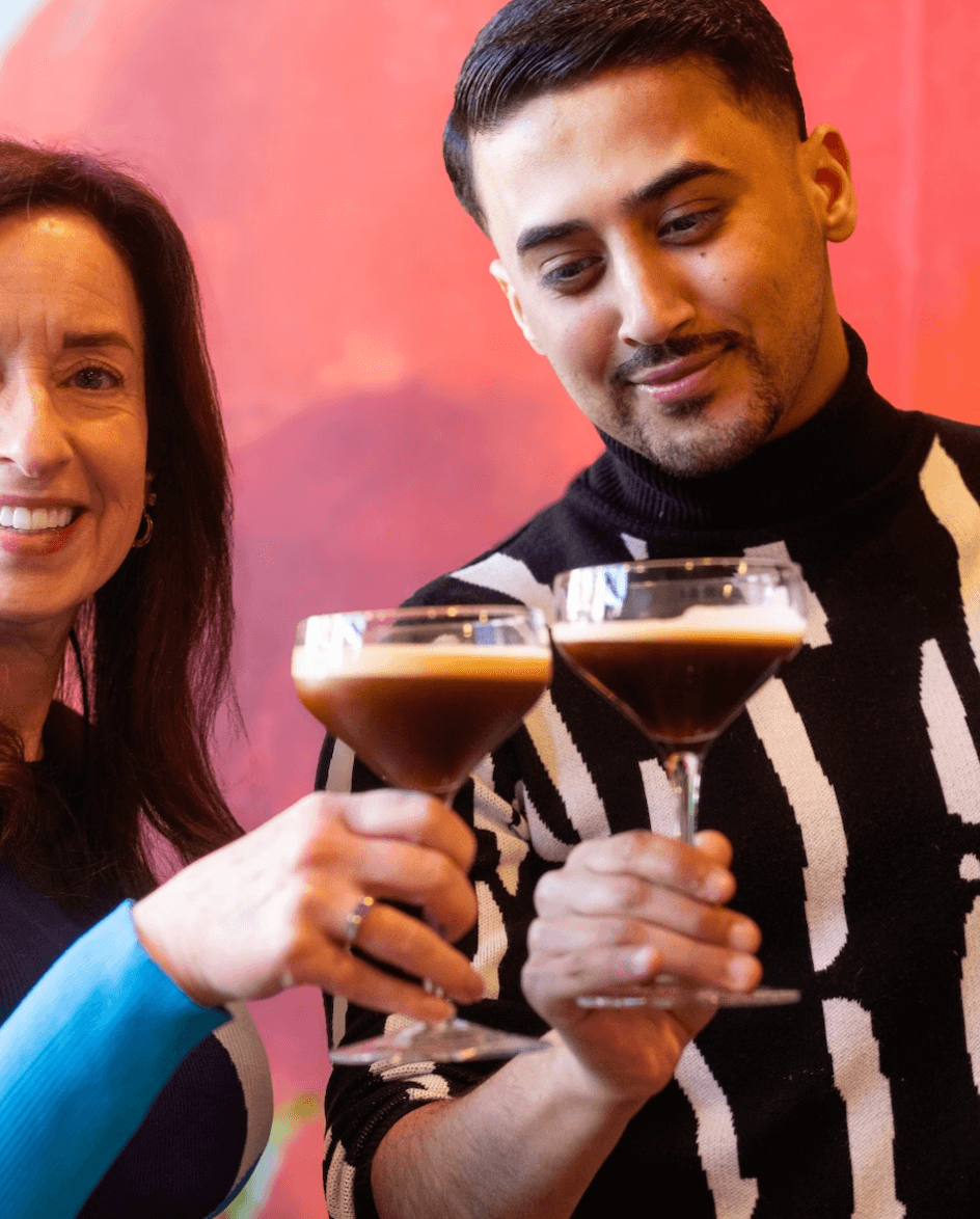 Your Updated Guide to South Main: A Hot Spot with Rich History - 5 A woman and a man clink cocktail glasses together, smiling, in front of a reddish background.