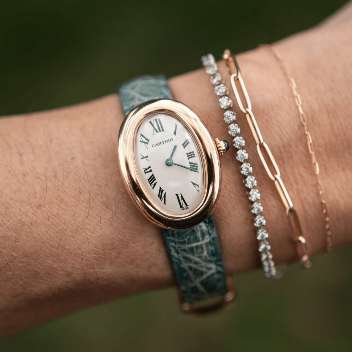 18 Nashville Luxe Loves: Statement Jewelry, Custom Hats & Summer Showstoppers - 10 A gold Cartier wristwatch with a blue patterned leather strap, worn on a wrist alongside two gold chain bracelets and a diamond bracelet.