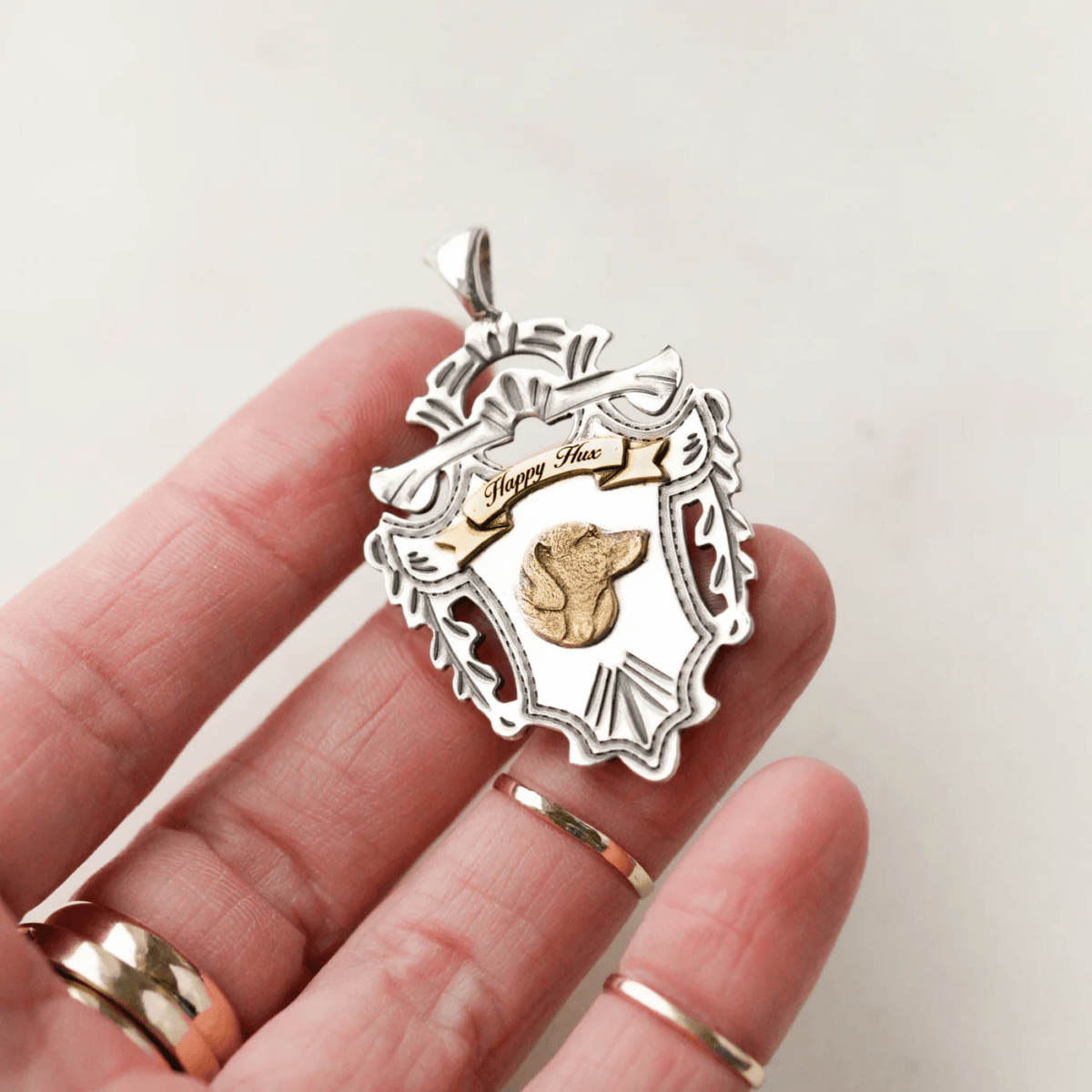 18 Nashville Luxe Loves: Statement Jewelry, Custom Hats & Summer Showstoppers - 8 A hand holding a luxe silver and gold crest-shaped pendant engraved and featuring a small gold animal head in the center—a perfect piece for anyone who loves unique style.