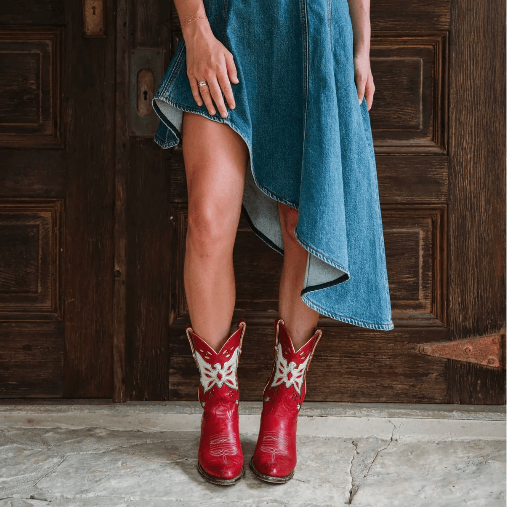 18 Nashville Luxe Loves: Statement Jewelry, Custom Hats & Summer Showstoppers - 6 Person who wears an asymmetrical denim skirt and red cowboy boots, standing on a stone floor in front of a wooden door.