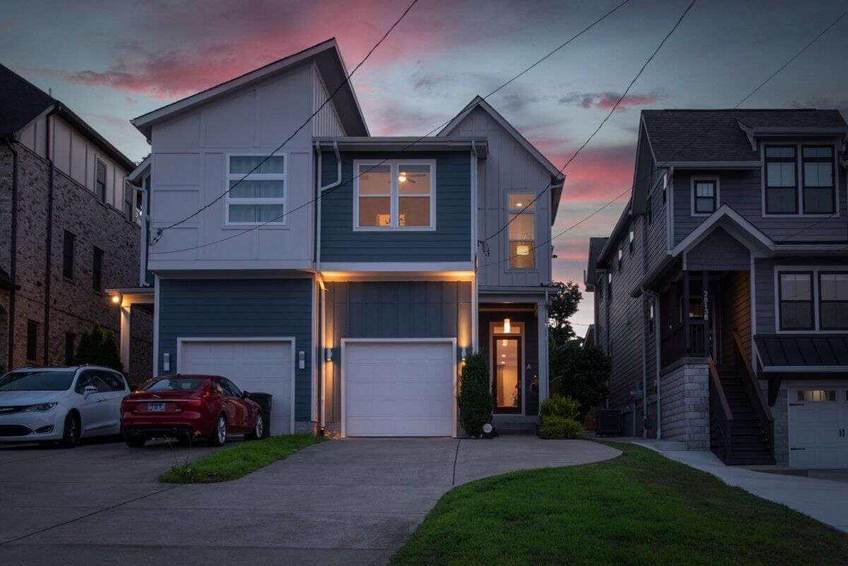 2815A W Kirkwood Ave, Nashville TN - 6 Modern two-story home at 2815A Kirkwood Ave, Nashville, featuring a single-car garage, driveway, and cars parked outside at dusk with neighboring homes visible on both sides.
