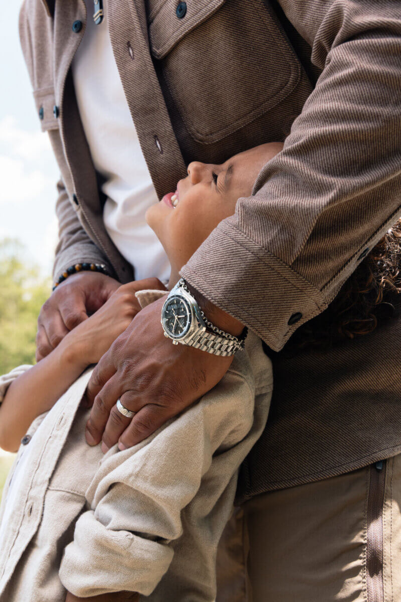 Personalized Jewelry Gifts for Life’s Biggest Milestones - 3 Adult embracing a smiling child outdoors, both in beige and brown clothing. The adult, wearing a wristwatch and diamond cellar fine jewelry, radiates warmth — perfectly capturing the spirit of thoughtful gifting.