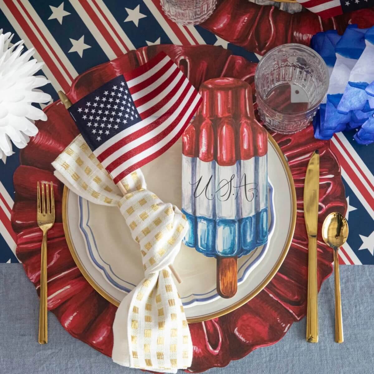 Nashville Steals, Deals & Announcements: July 2026 - 6 A table setting with a USA-themed plate featuring a rocket popsicle, gold utensils, an American flag napkin, and patriotic decorations in red, white, and blue.