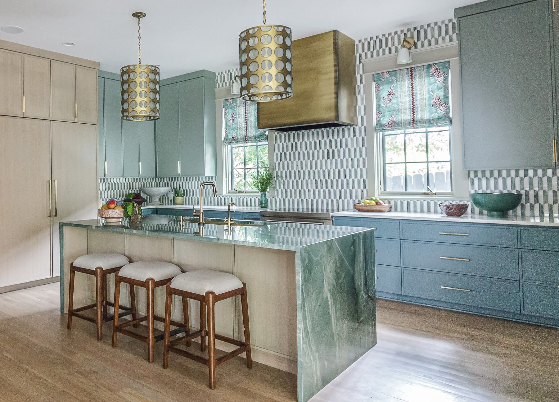 Modern kitchen with a marble island, three upholstered stools, blue cabinets, and a patterned backsplash—showcasing the refined touch you get when you hire an interior designer to guide your interior design process.