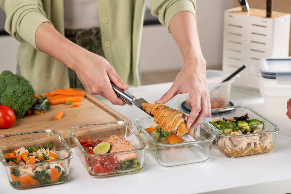 Not All Proteins Are Created Equal! Here's How to Eat for Your Goals - 2 A person slices chicken breast and prepares healthy, high-protein quality meals in glass containers on a kitchen counter with vegetables and salmon.