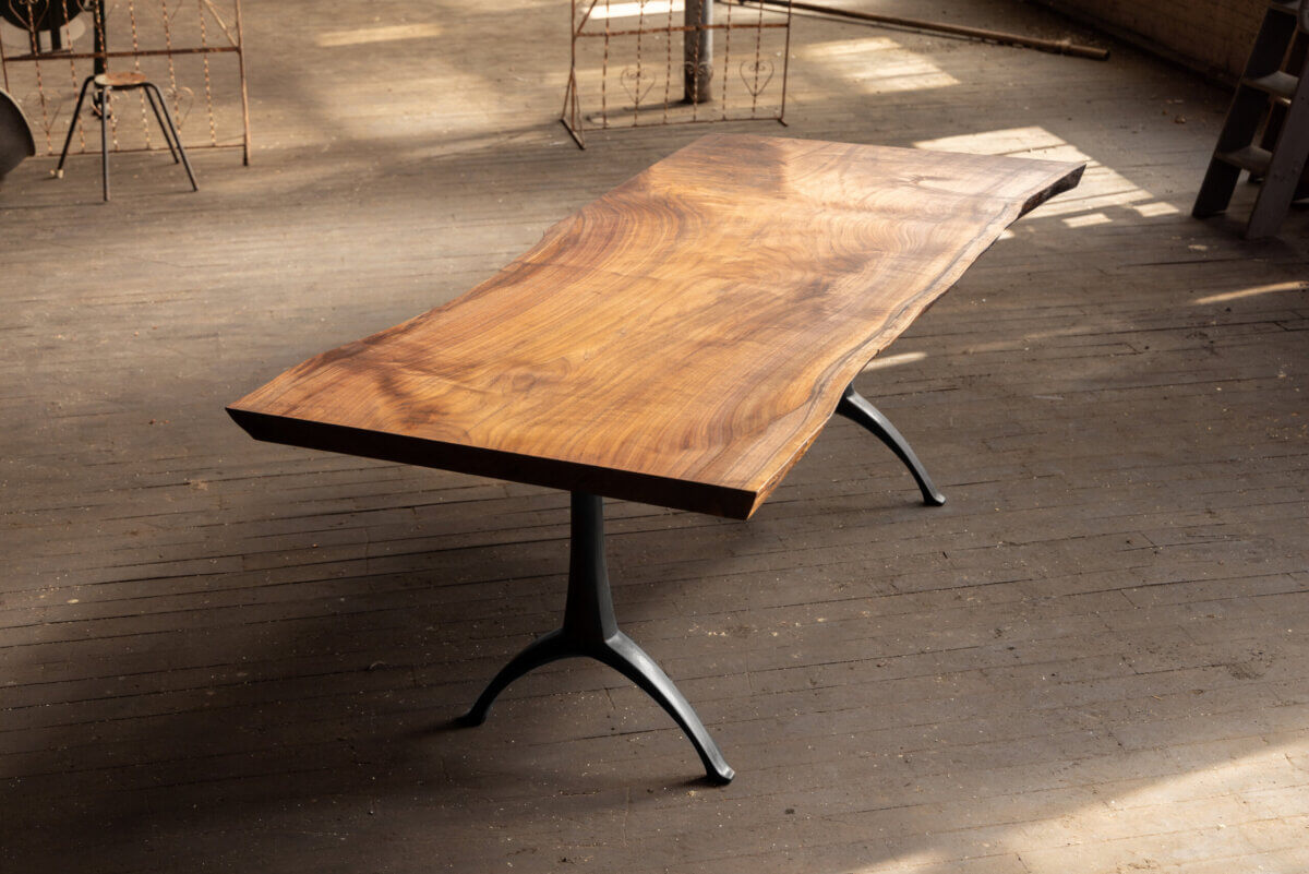 Turning Fallen Trees into Fine Furniture: The Art of Alabama Sawyer - 5 A live-edge wooden table with a metal base stands on a wooden floor in a sunlit room.
