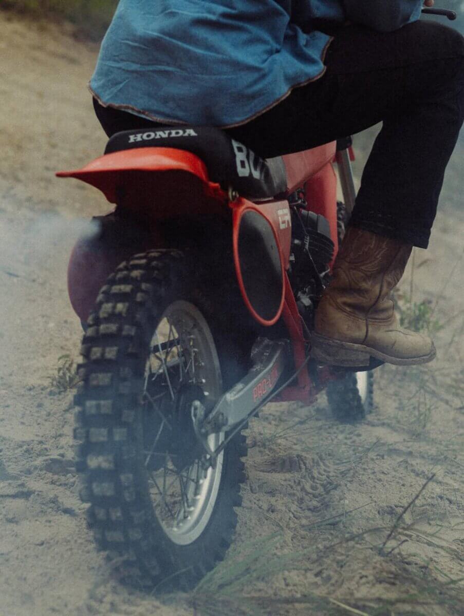 This Mississippi-Based Boot Company Should Be on Your Radar - 8 Person wearing brown boots rides a red Honda dirt bike on sandy terrain, rear tire kicking up dustβa scene that echoes western style and Mississippi roots.