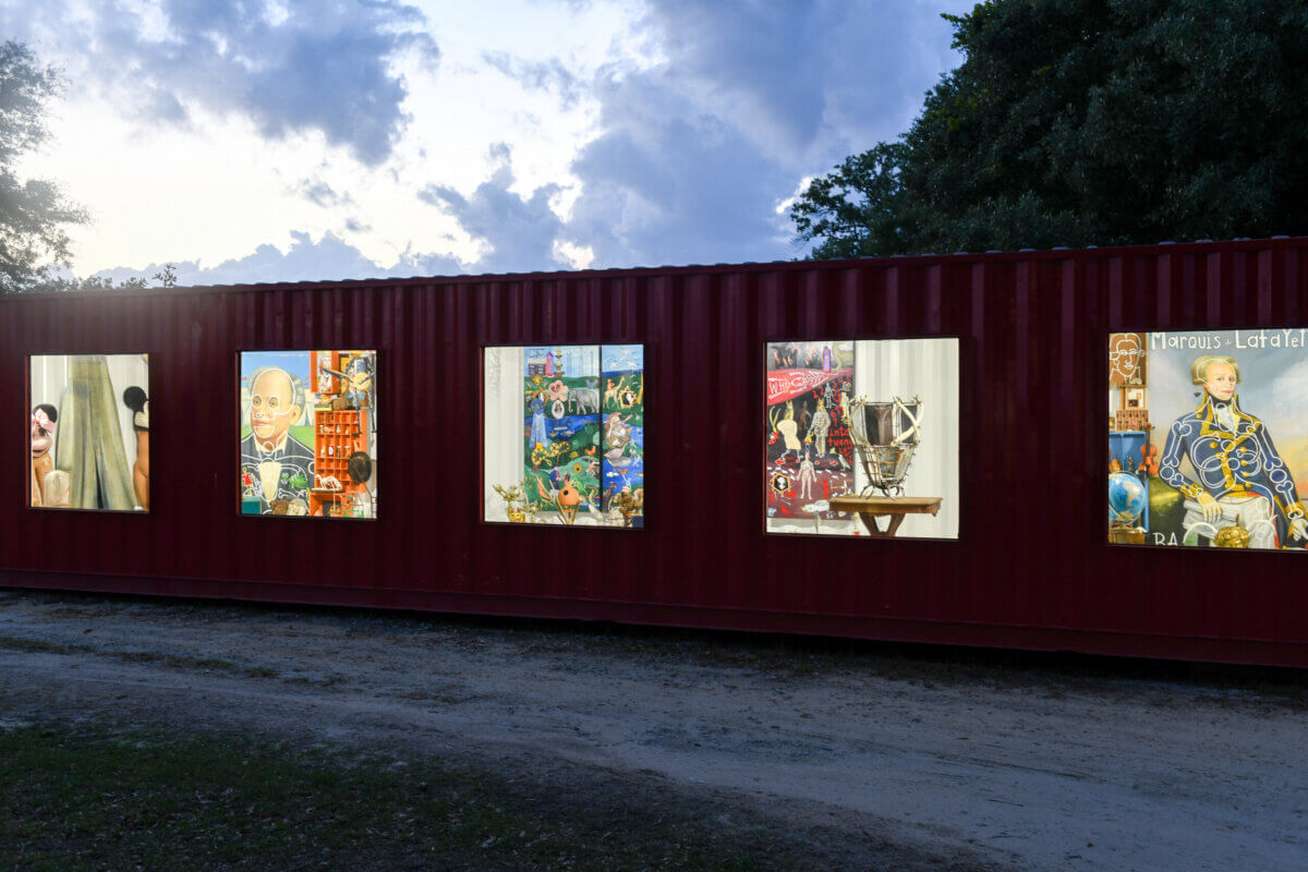 Inside Alabama Artist Butch Anthony's "Museum of Wonder" - 5 A red shipping container with illuminated windows displays various colorful artworks and objects inside at dusk at Butch Anthony's Museum of Wonder.