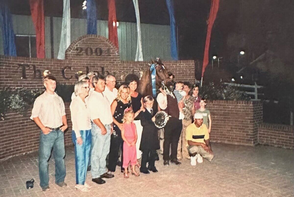 This Mississippi-Based Boot Company Should Be on Your Radar - 3 A group of people, including children, pose in front of a brick wall with a horse and a trophy at night; red, white, and blue banners hang above, reflecting classic Western style and proud Mississippi roots.