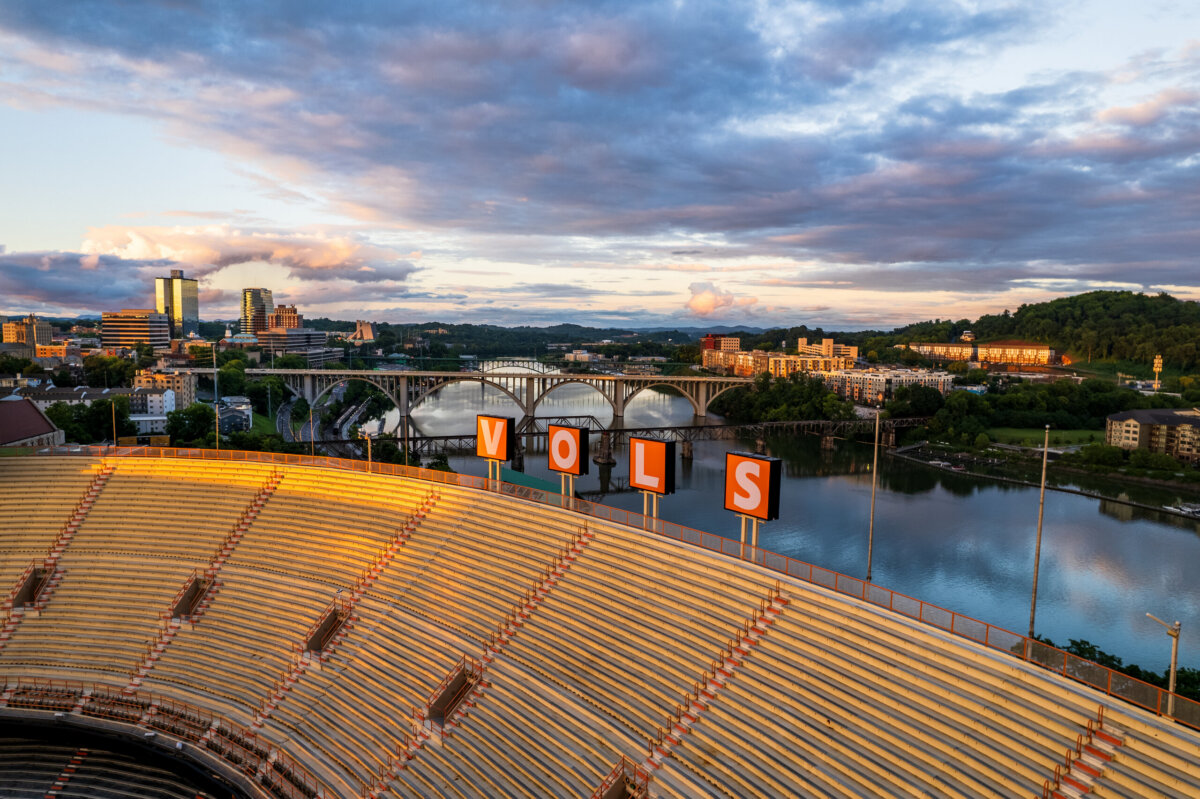 Aerial view of a stadium with "VOLS" sign, overlooking a river, bridge, and cityscape under a partly cloudy sky—one of the Top SEC Towns featured in the 2026 Update.