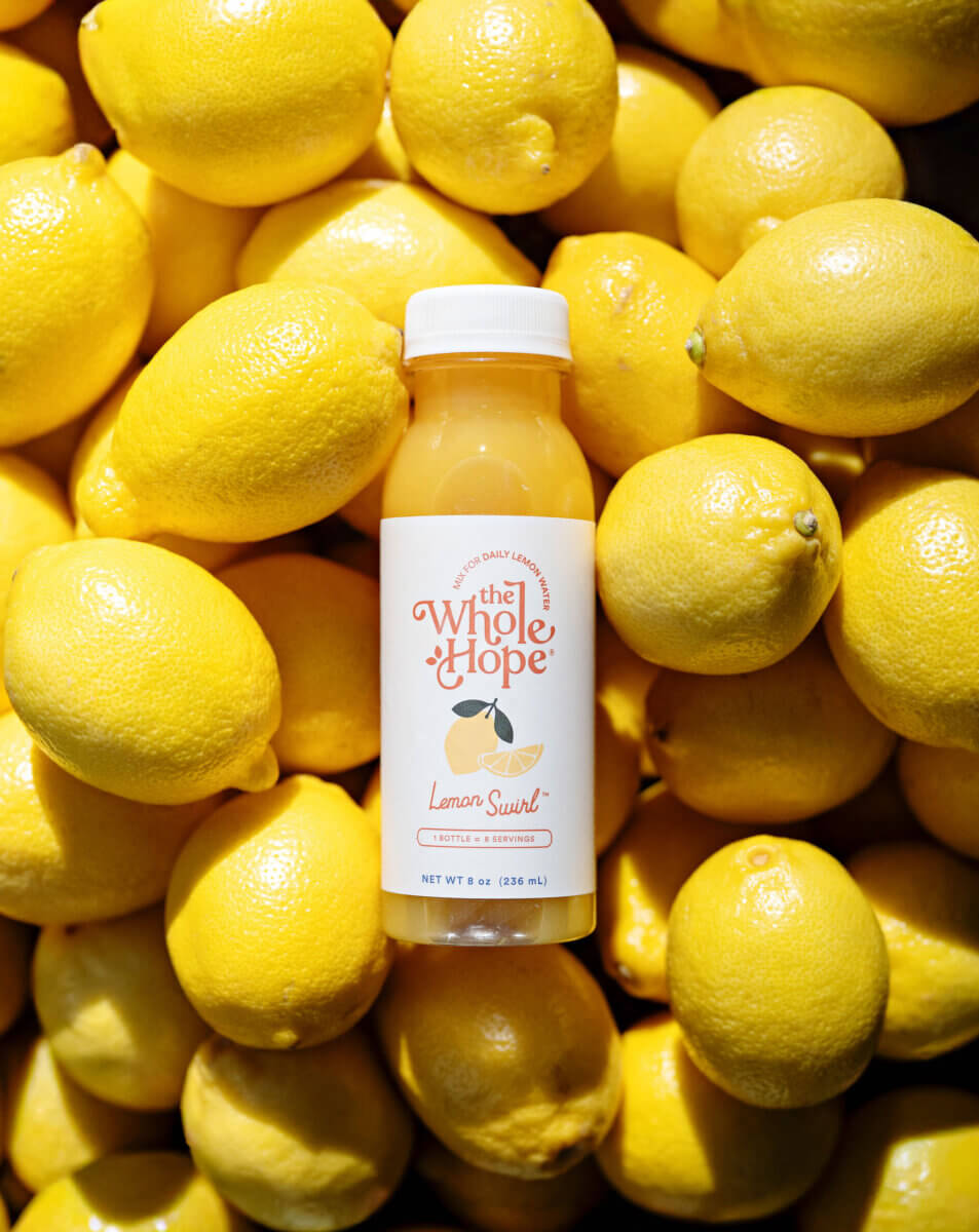 Trusting Her Gut: Meet the Charlotte Woman Making Healthy Habits Easier - 8 A bottle of The Whole Hope Lemon Swirl drink is placed upright on a pile of fresh yellow lemons.