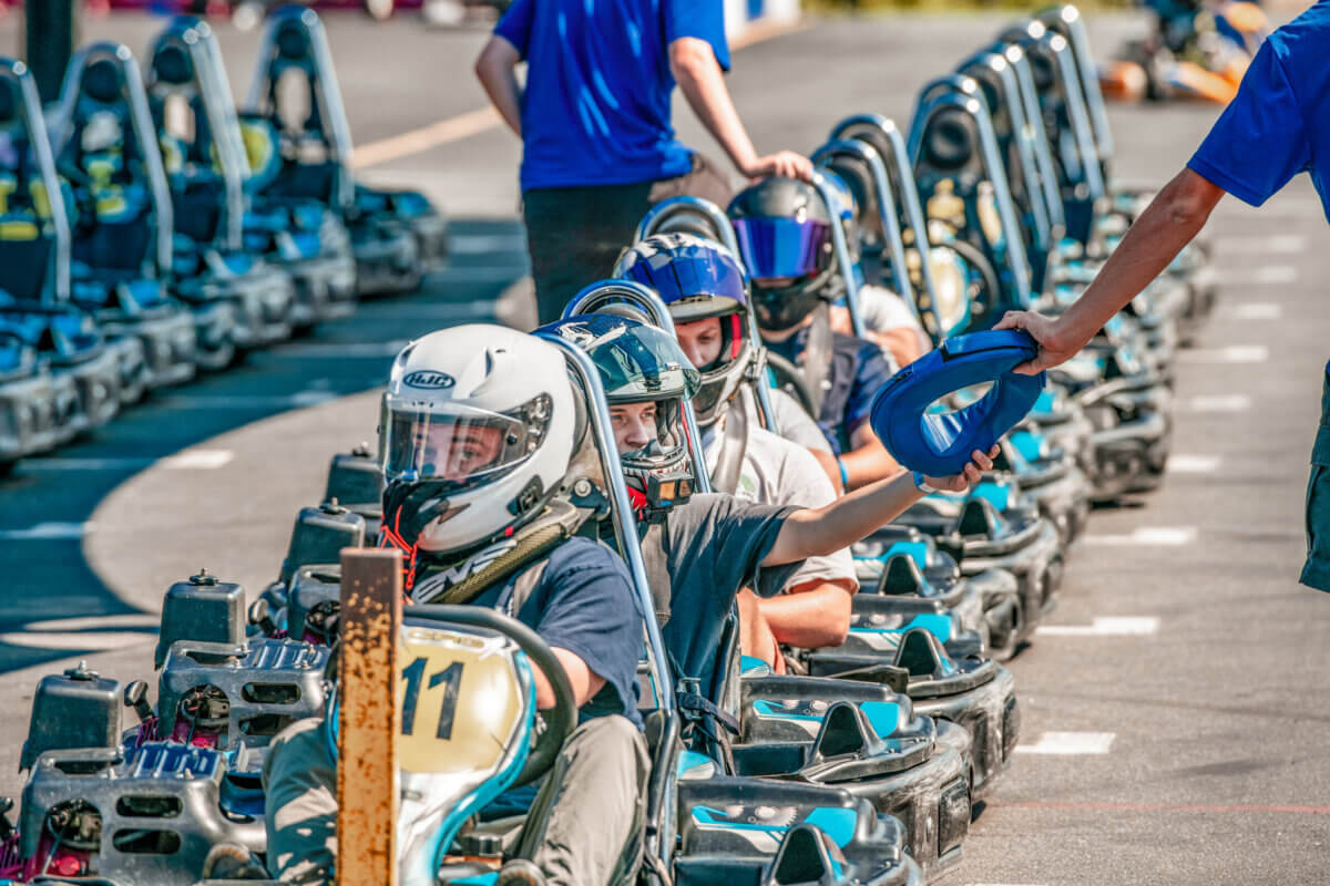 Great Southern Outdoors: Destinations for Active Travelers - 5 Active travelers gather in helmets, seated in go-karts lined up outdoors at the Great Southern Outdoors, as one racer reaches out to take a blue object from a standing official.