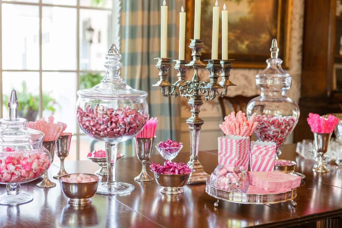 A table at the Kappa Alpha Theta sorority house is set with glass jars and bowls filled with pink candies, striped treat bags, and a silver candelabra with unlit candles.