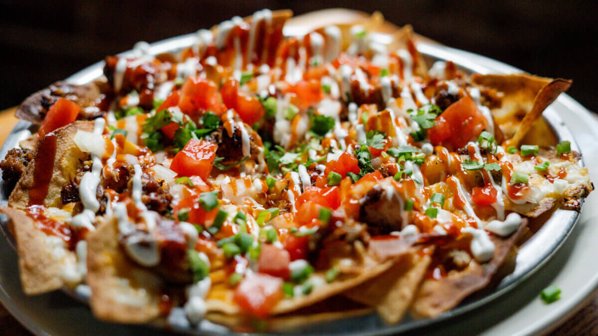 A plate of nachos topped with diced tomatoes, jalapeños, ground meat, melted cheese, and drizzled with sour cream and sauce—perfect for a summer getaway or your next travel stop in Tupelo MS.