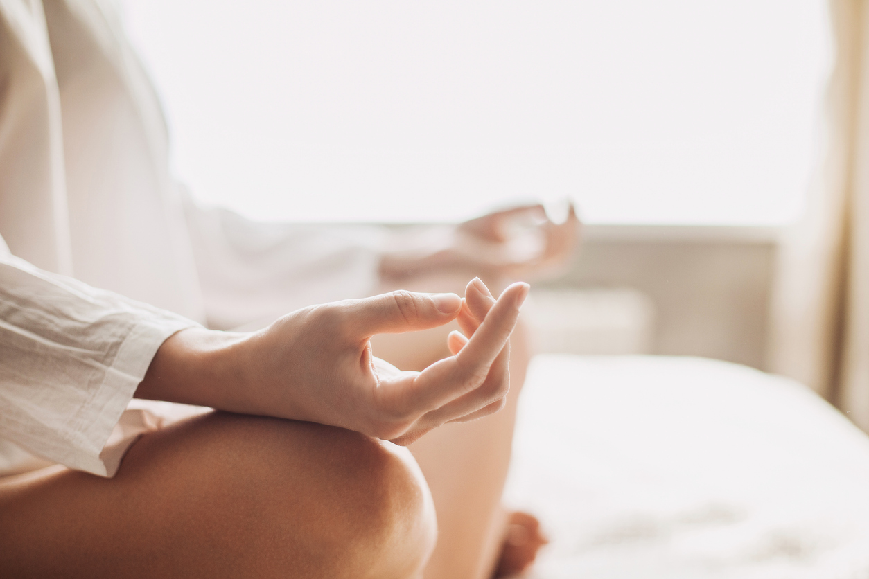 A person sits cross-legged on a bed, wearing a white robe, with hands resting on knees in a meditation pose, reflecting on the path to financial peace.