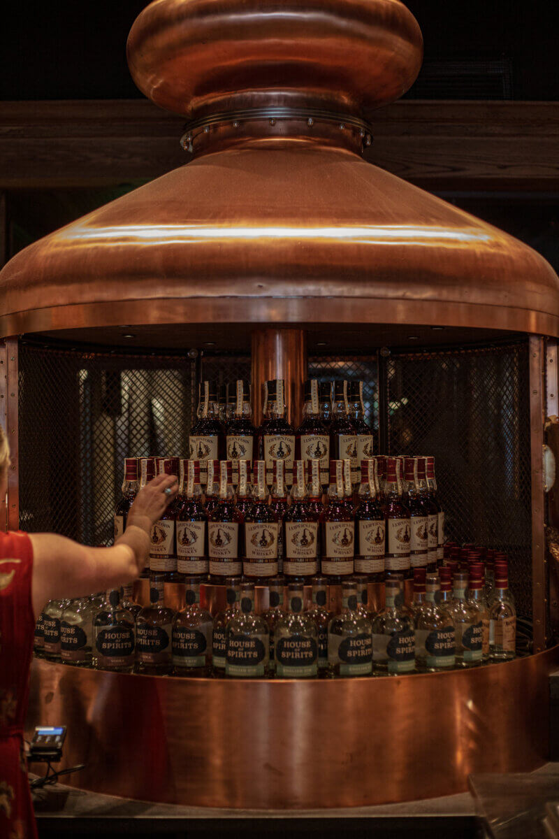 From Farm Life to Fine Spirits: Meet the Co-Owner of Leiper's Fork Distillery - 5 A person reaches towards a display of liquor bottles arranged in tiers inside a large copper still at Leiper's Fork Distillery.