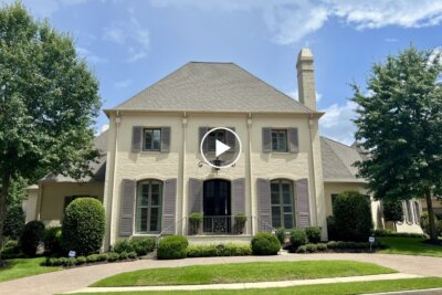 Two-story beige house with grey shutters, tall windows, a central front door, and manicured shrubs at 2360 Mont Alban Cv in Germantown TN—ideal real estate set against a blue sky with scattered clouds.