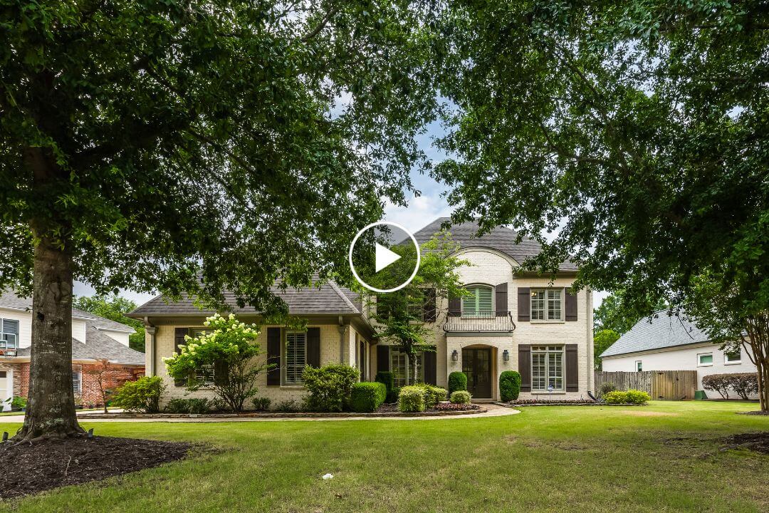 A two-story brick house with dark shutters and a landscaped front yard, partially shaded by large trees, in the suburban Germantown TN neighborhood of Dogwood Creek Dr.